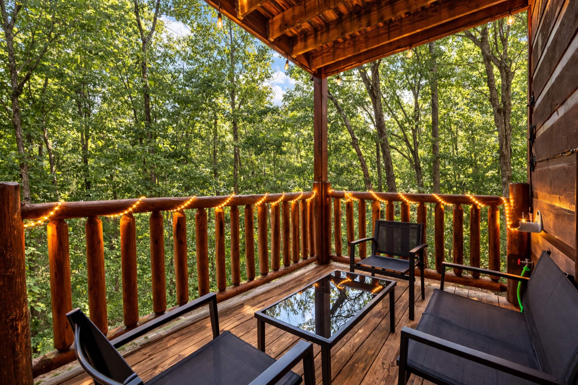 Covered lower deck at Bearadise with patio seating, a glass top table, and log railing strung with lights